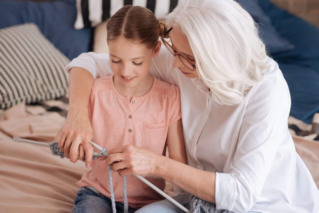 Grandmother sits with her happy granddaughter as she helps teach her to knit. Contact our skilled Idaho guardianship lawyer to help you navigate through the complex process of gaining guardianship.