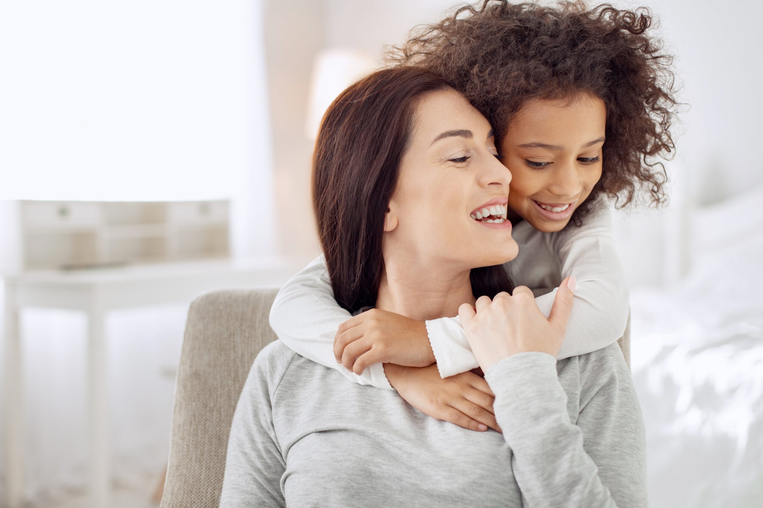 Woman sits on chair with a happy child’s arms around her. Get in touch with our skilled Boise guardianship lawyer to help you through the complex journey of gaining guardianship.