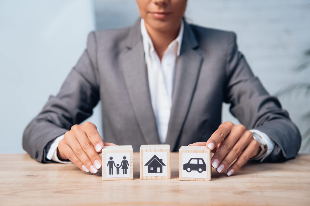 Cropped view of a woman touching wooden cubes with images of a family, a car, and a house. Take out the stress of dividing assets after a divorce and contact our experienced high asset divorce attorneys for legal support.