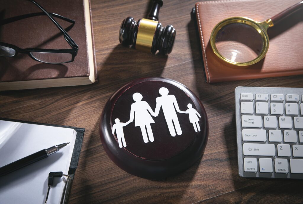 Paper cut family lays next to various items, a justice gavel, magnifying glass, and a book. Call us for an experienced Canyon County, ID family law lawyer if you are going through a divorce or child custody battle.