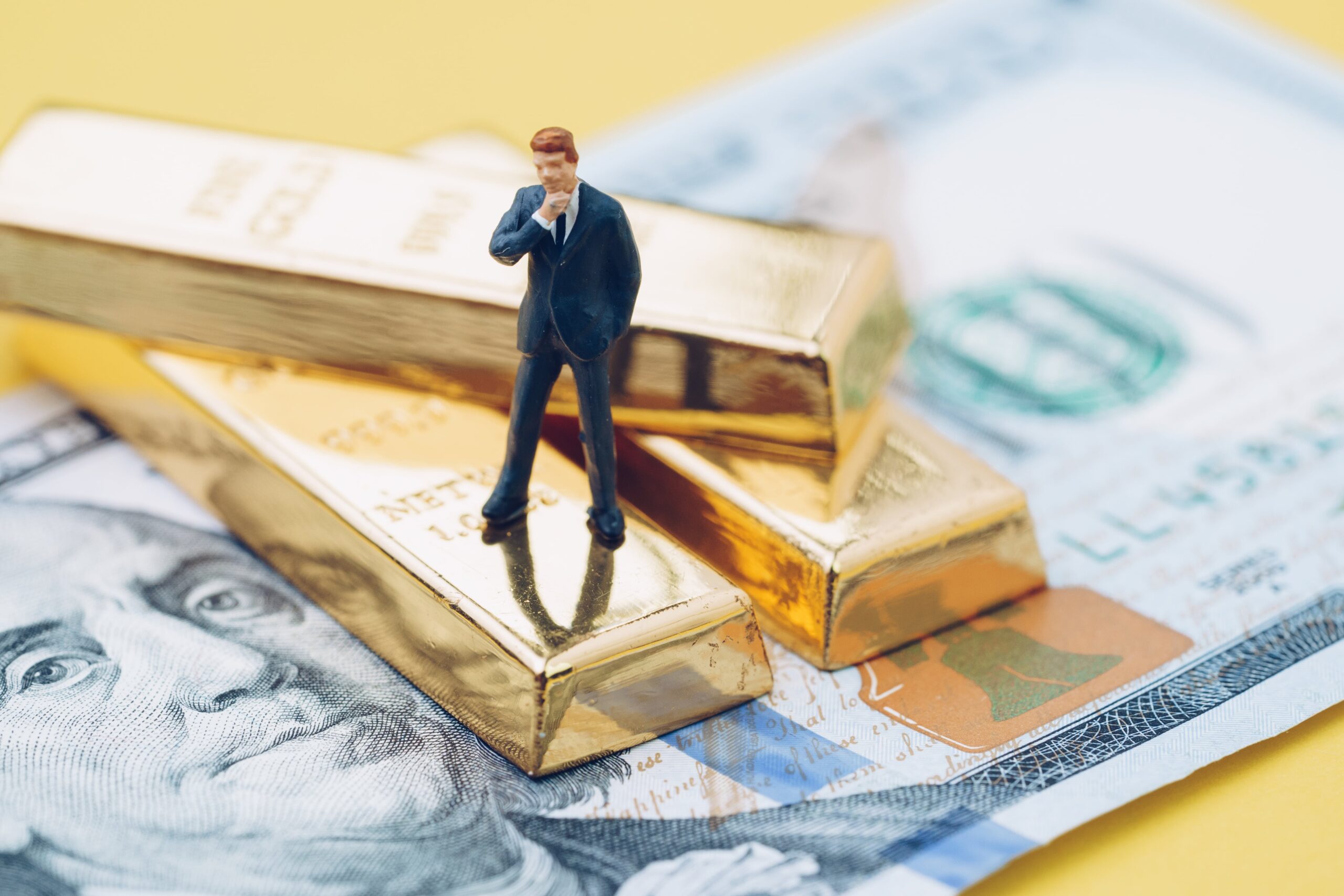 Figure of a man in a suit stands on top of gold bars and cash. Contact us for a Boise high asset divorce attorney who understands asset division in a divorce. 