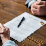 partial view of lawyer and client sitting at table with divorce decree and wedding rings