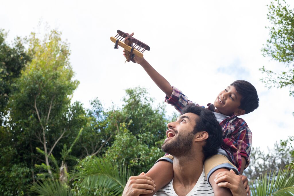 Child on a parent's shoulders playing with a plane toy